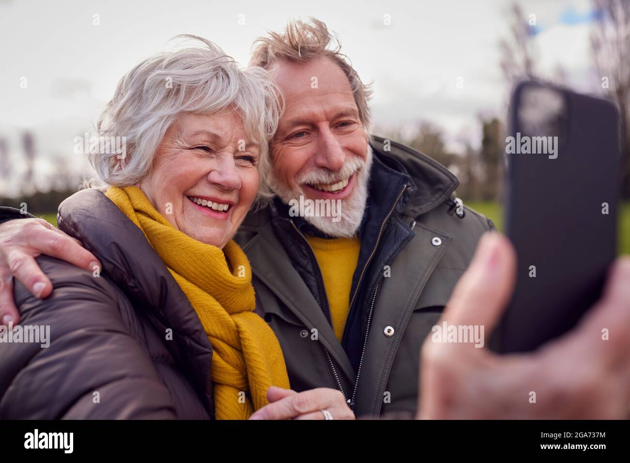 Couple Senior aimant posant pour Selfie sur téléphone mobile en automne ou en hiver à travers le parc Banque D'Images