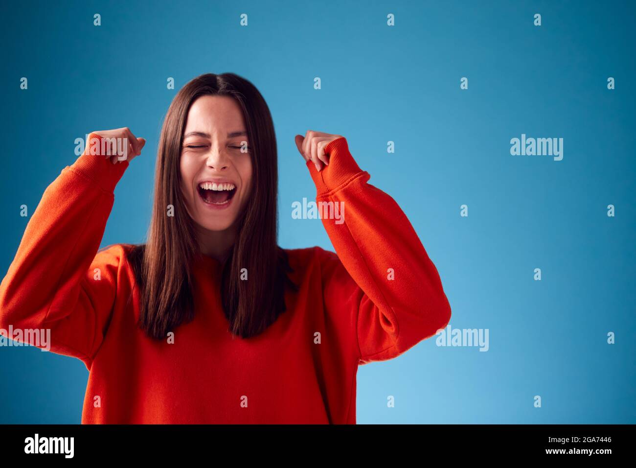 Jeune femme excitée célébrant et pompant les poings dans l'air contre le bruit de fond du studio bleu Banque D'Images