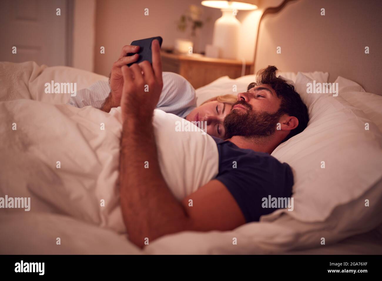Couple avec un homme allongé au lit la nuit regardant l'écran du téléphone  portable Photo Stock - Alamy