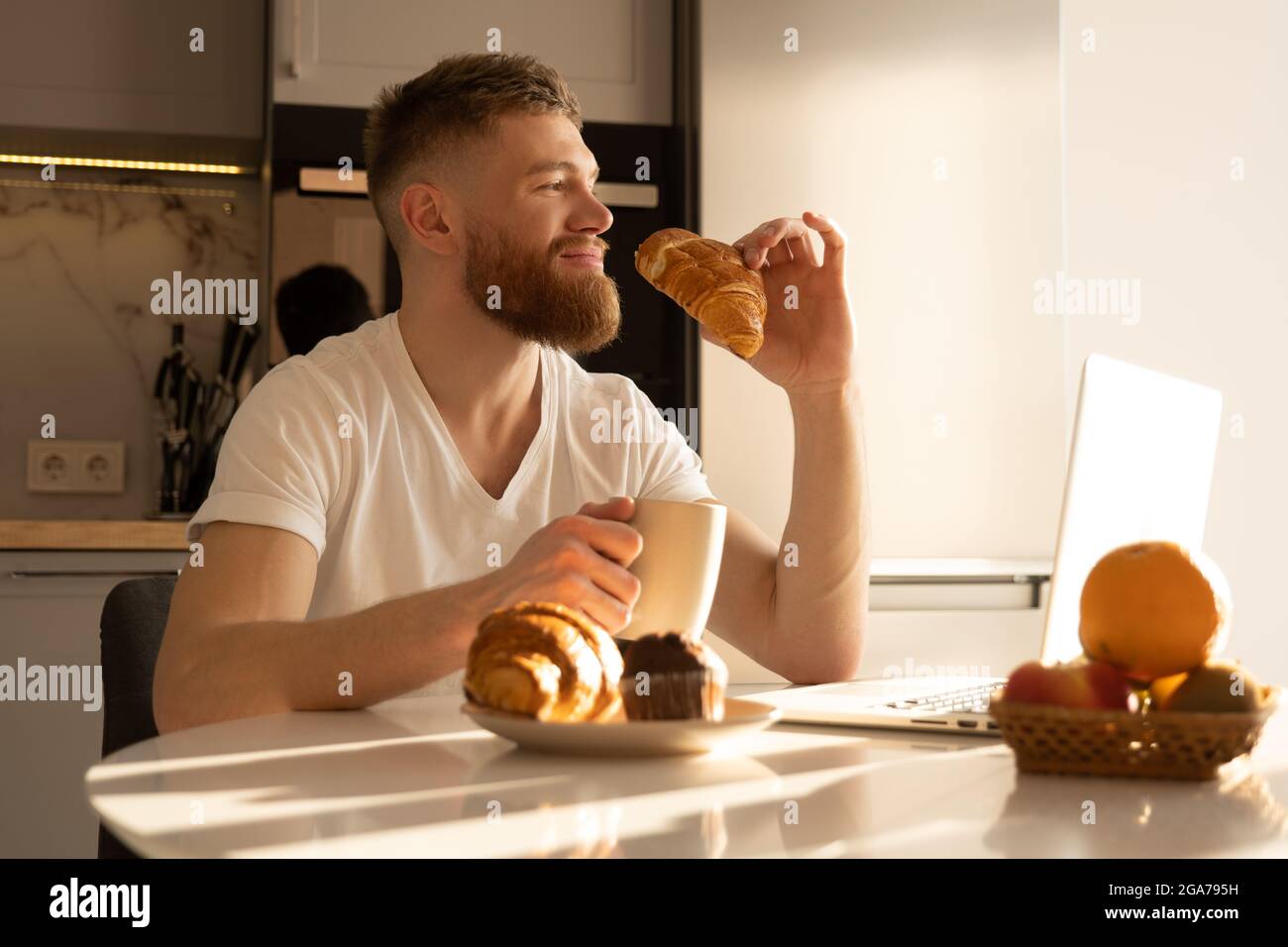 Homme mangeant un croissant et prenant du thé au petit déjeuner Banque D'Images