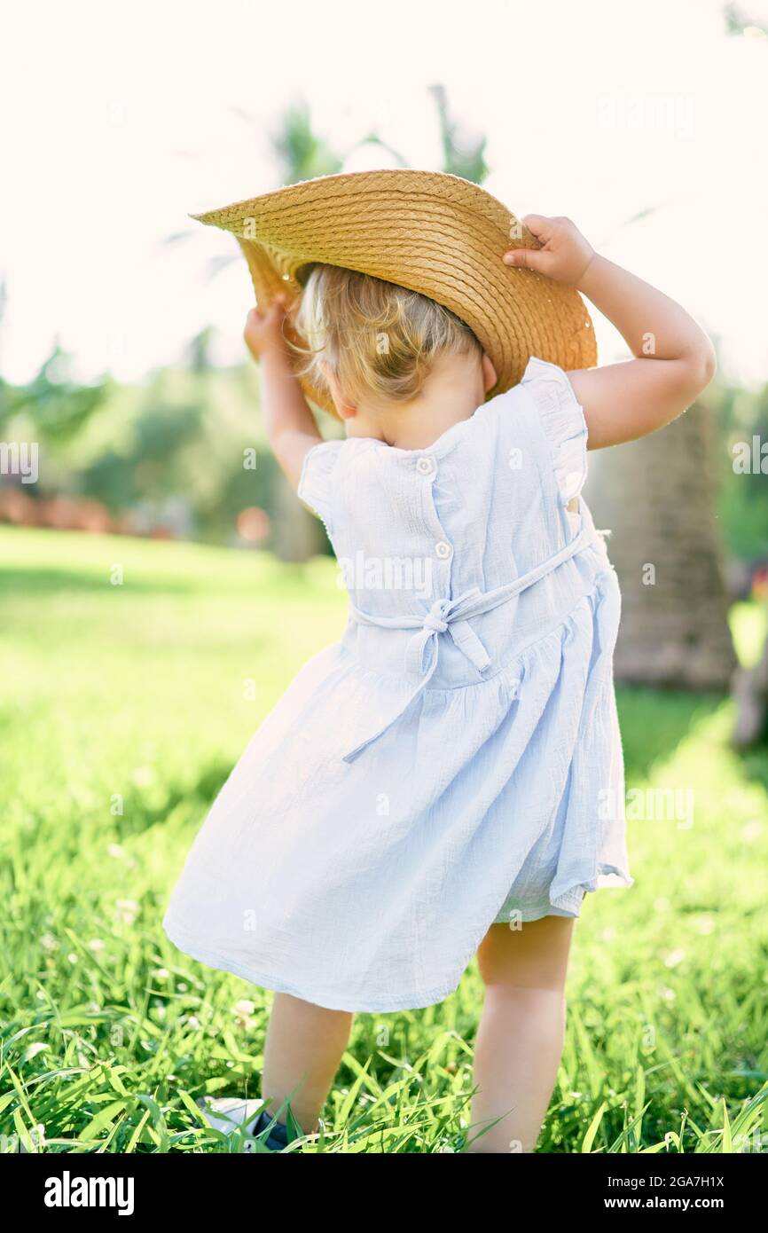 Une petite fille met un chapeau tout en se tenant sur une pelouse verte. Vue arrière Banque D'Images