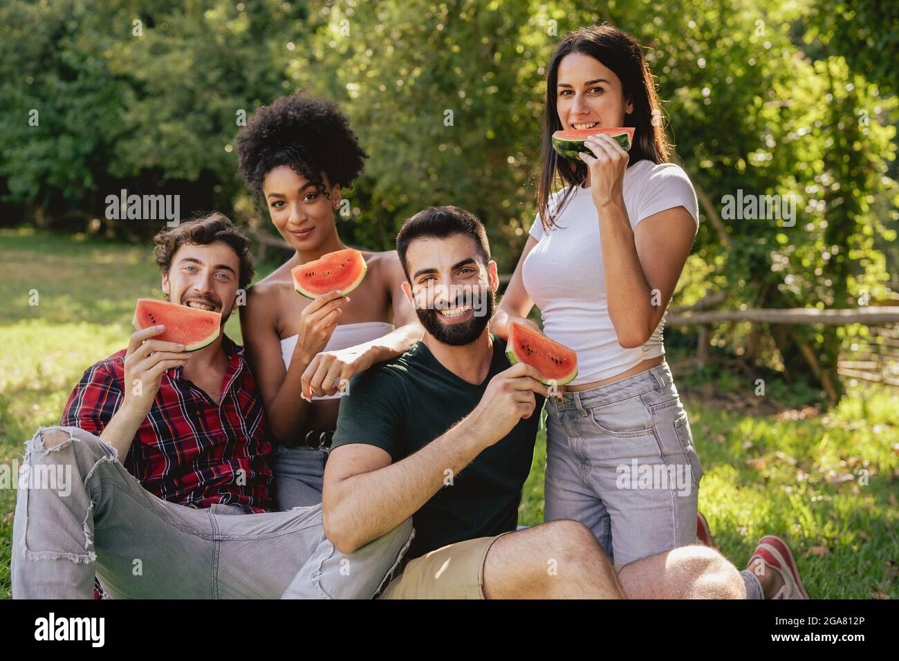 Portrait de jeunes multiraciaux mangeant de la pastèque à l'extérieur dans la campagne et regardant l'appareil photo. Banque D'Images