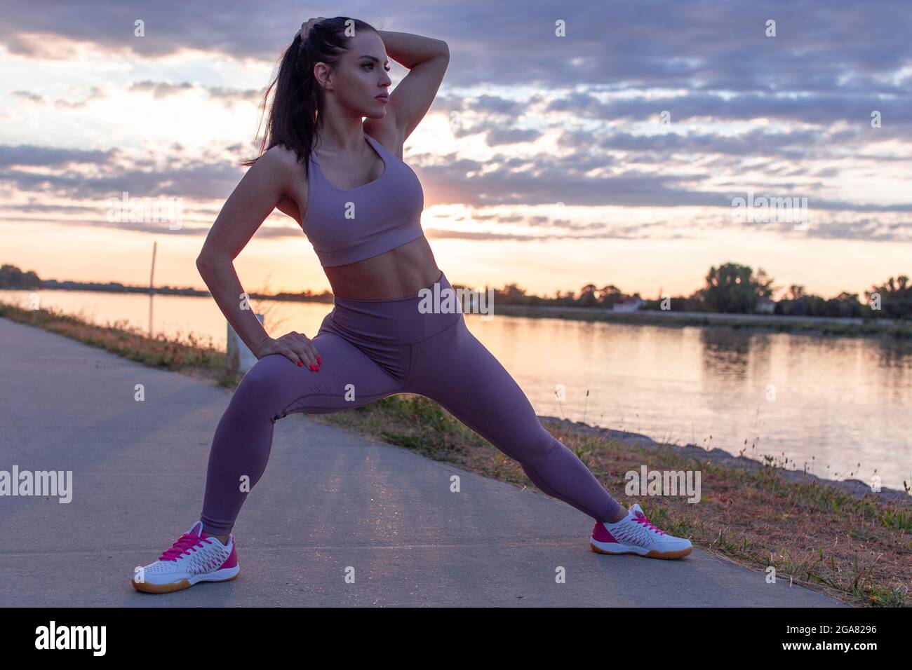 Jeune femme caucasienne s'étirant avant de courir, réchauffez-vous de l'exercice au lever du soleil, en regardant loin Banque D'Images