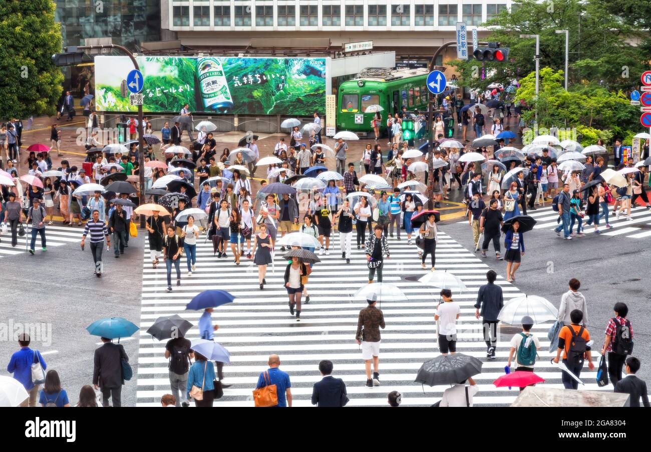 Tokyo, Japon - 21 juin 2016 : les rues animées de Tokyo par un jour de pluie. De nombreuses personnes portant des parasols traversent l'intersection très fréquentée de Shibuya Crossing. Banque D'Images