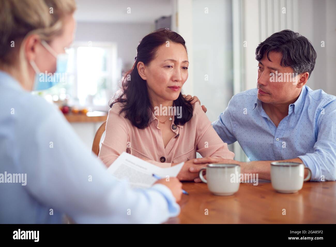 Un couple asiatique adulte inquiet à la réunion à domicile avec une travailleuse de soins de santé féminine dans le masque pendant une pandémie Banque D'Images