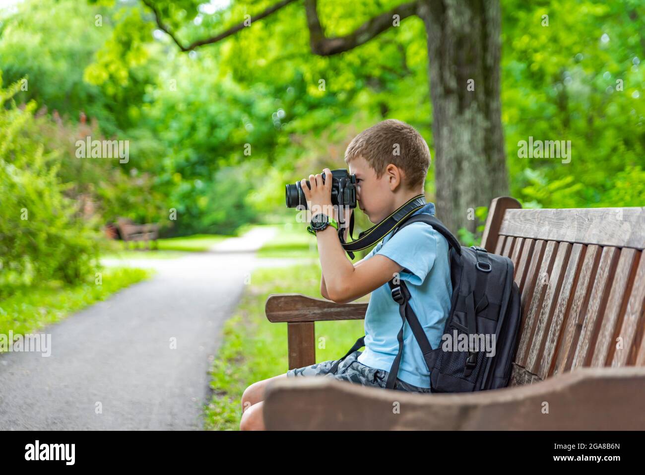 Tourisme avec un appareil photo. Un garçon avec un appareil photo prend des photos de la nature dans le parc. Un jeune photographe s'assoit sur un banc de parc et prend des photos de Banque D'Images