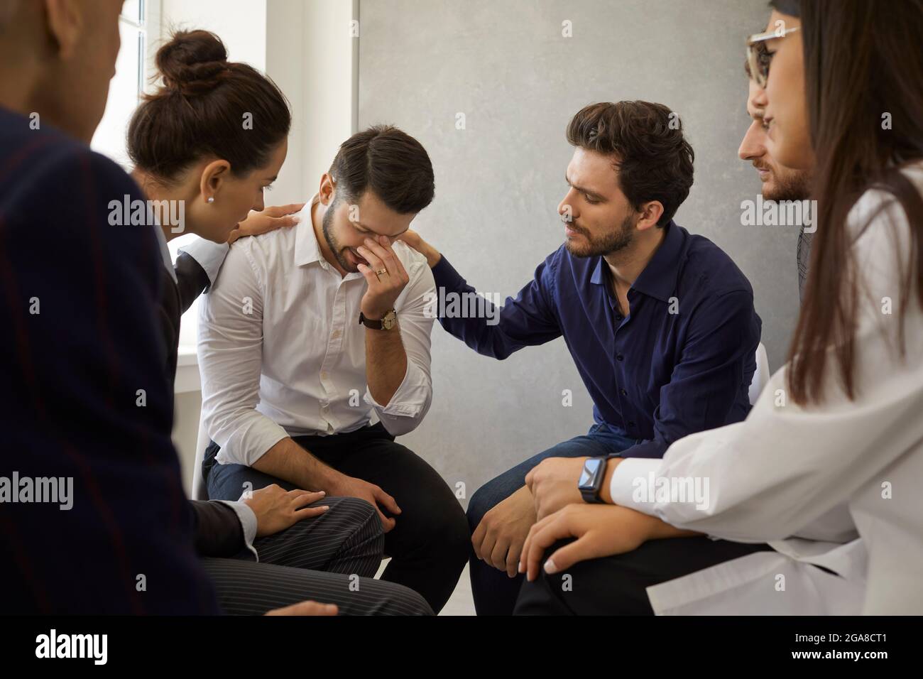 Les gens dans une réunion de thérapie de groupe réconfortant et soutenant un jeune homme déprimé Banque D'Images
