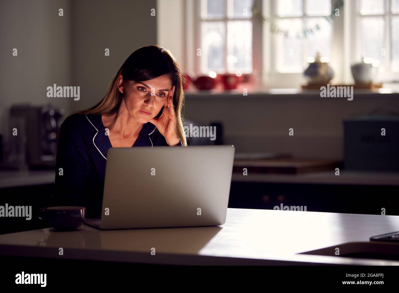 Femme malheureuse portant un pyjama assis dans la cuisine la nuit en utilisant un ordinateur portable Banque D'Images