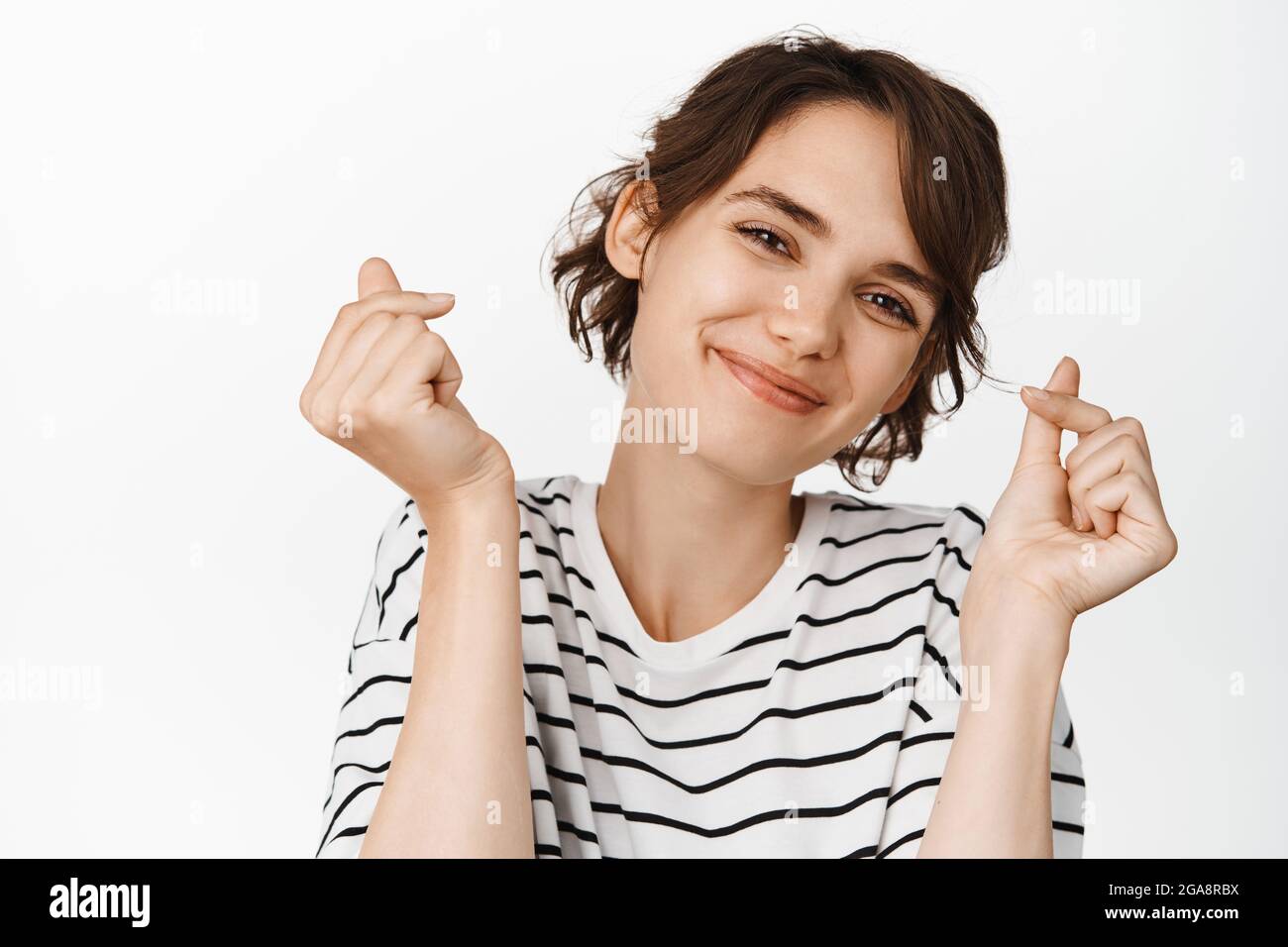 Belle fille moderne, jeune femme sans maquillage, peau claire et brillante, danse et sourire, debout dans un t-shirt sur fond blanc Banque D'Images