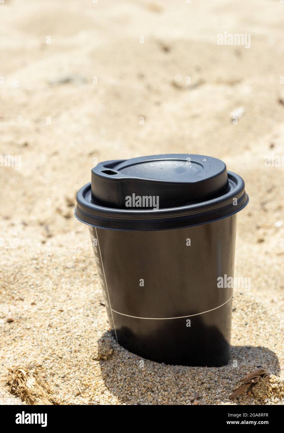 Tasse à café jetable en plastique noir sur le sable Banque D'Images