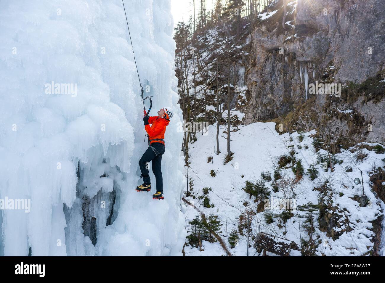L'athlète masculin monte la falaise couverte de glace, balançant la hache de glace et en utilisant des crampons pour prendre un pied Banque D'Images
