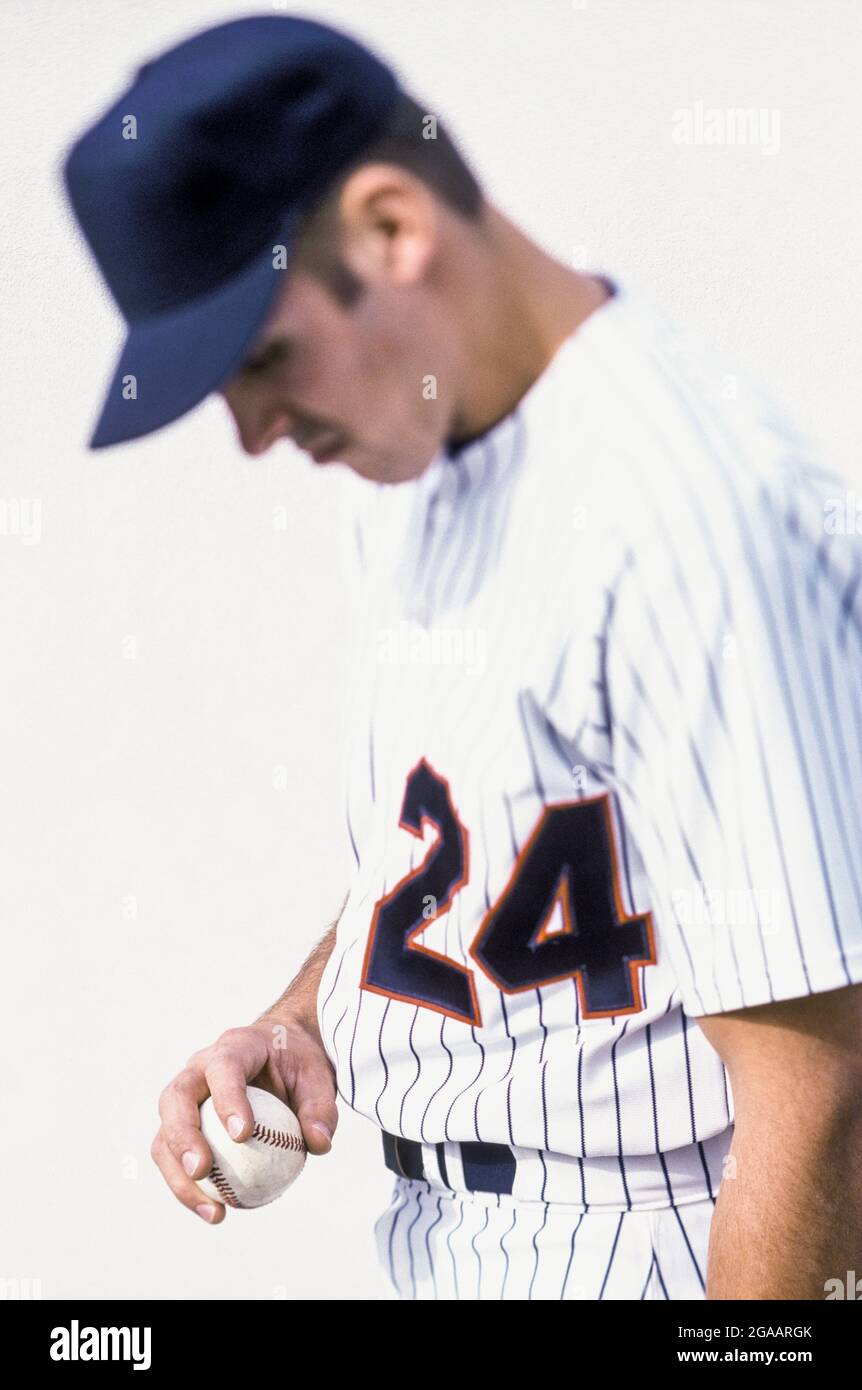 Un joueur de baseball en uniforme regardant le baseball dans sa main. Banque D'Images