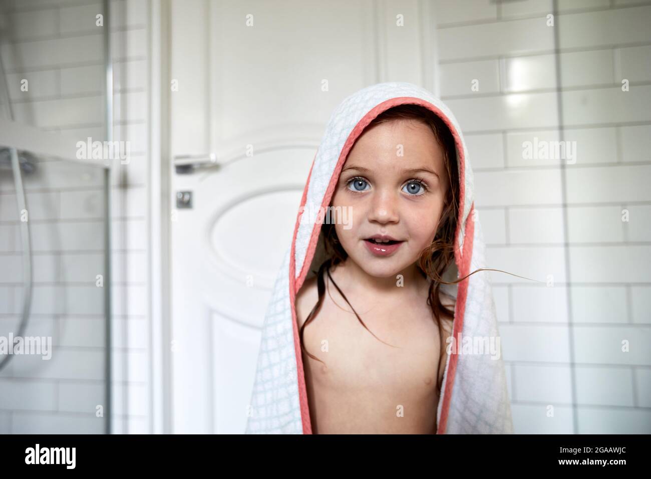 Mignon enfant avec les cheveux mouillés et dans le peignoir debout dans la salle de bains après avoir pris la douche et regarder l'appareil photo Banque D'Images