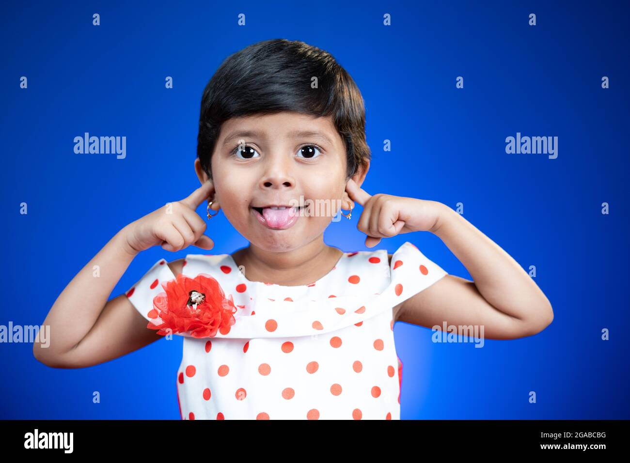 Petite fille enfant avec la langue dehors ou grimacing dansant sur fond bleu - heureux, gai et fou concept d'enfants. Banque D'Images