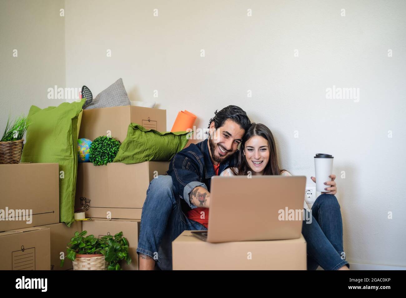 Un jeune couple heureux déménagent dans une nouvelle maison tout en utilisant un ordinateur portable pour faire du shopping en ligne Banque D'Images