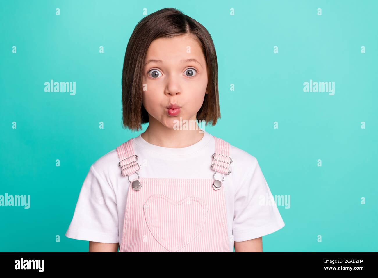 Photo de drôle funky heureuse petite fille envoyer air baiser visage gai isolé sur pastel teal couleur fond Banque D'Images