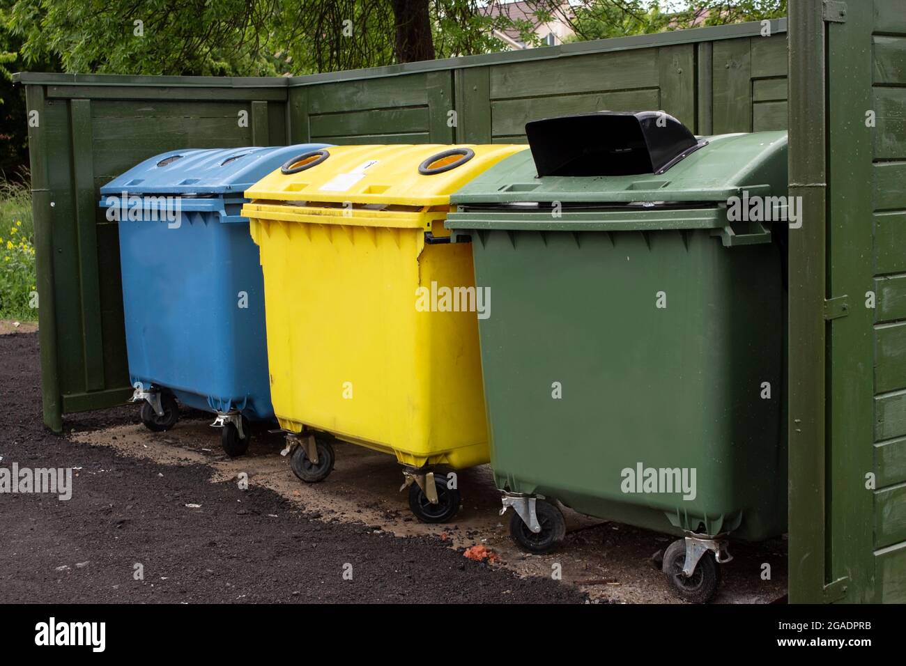 Trois conteneurs en plastique de plusieurs couleurs avec déchets près de la clôture. Collecte séparée des déchets ménagers. Attitude responsable envers l'environnement. Banque D'Images