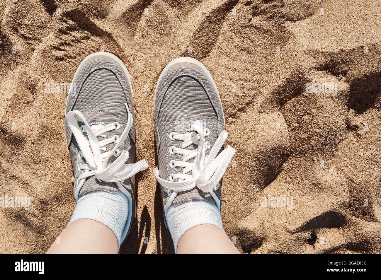 Jambes en baskets grises sur le sable de la plage. Concept de vacances d'été au bord de la mer. Voyage de style de vie. Vue POV. Copier l'espace. Banque D'Images