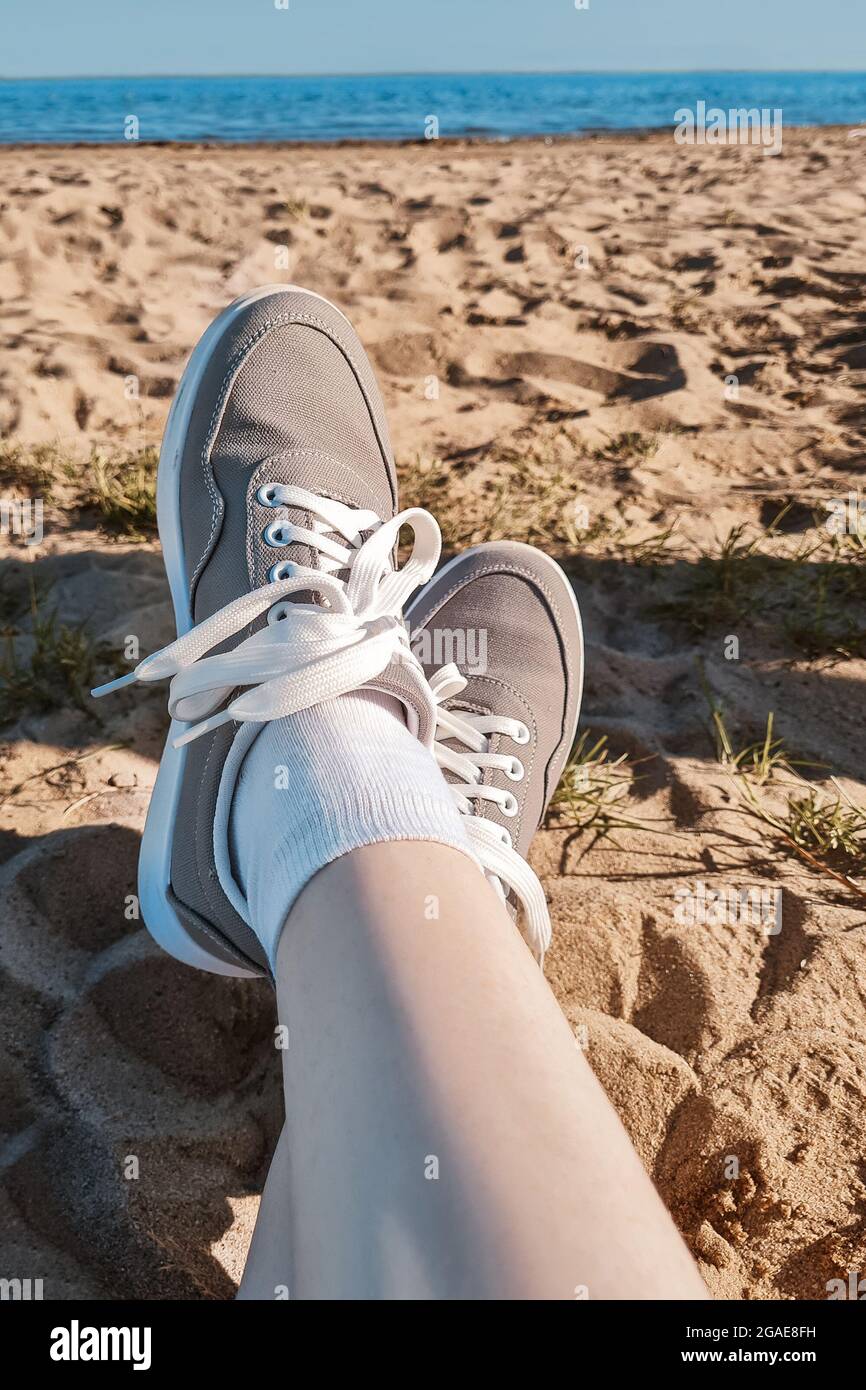 Jambes en baskets grises sur le sable de la plage. Concept de vacances d'été au bord de la mer. Voyage de style de vie. Vue POV. Copier l'espace. Banque D'Images