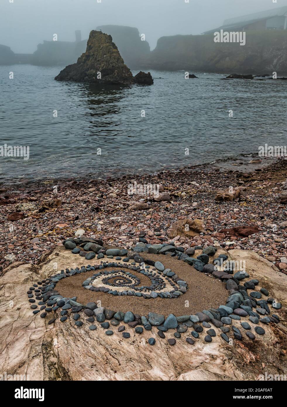 Sculpture en pierre ou en pierre, motif en spirale sur la plage avec une pile de mer le jour de la brume, Dunbar, East Lothian, Écosse, Royaume-Uni Banque D'Images