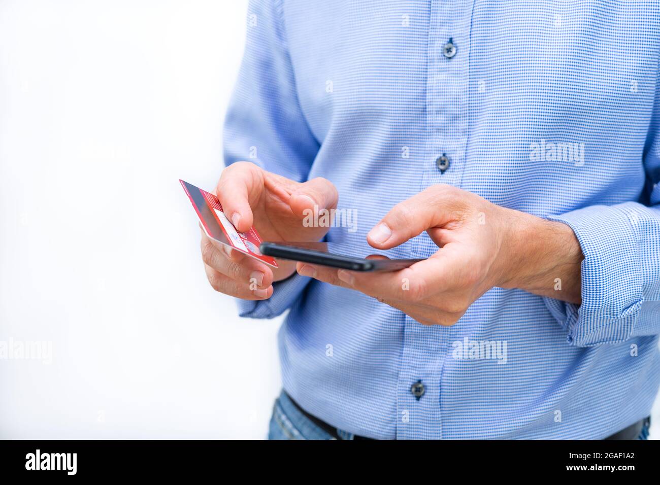 Homme avec téléphone et carte de crédit dans les mains et chemise bleue sur fond blanc. Copier l'espace. Banque D'Images