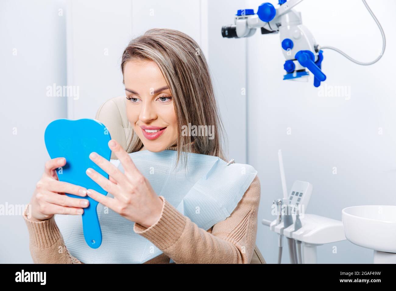 Bonne femme attirante regardant ses dents dans le miroir. Patient satisfait de soins dentaires ou de blanchiment pour le traitement dentaire. Banque D'Images