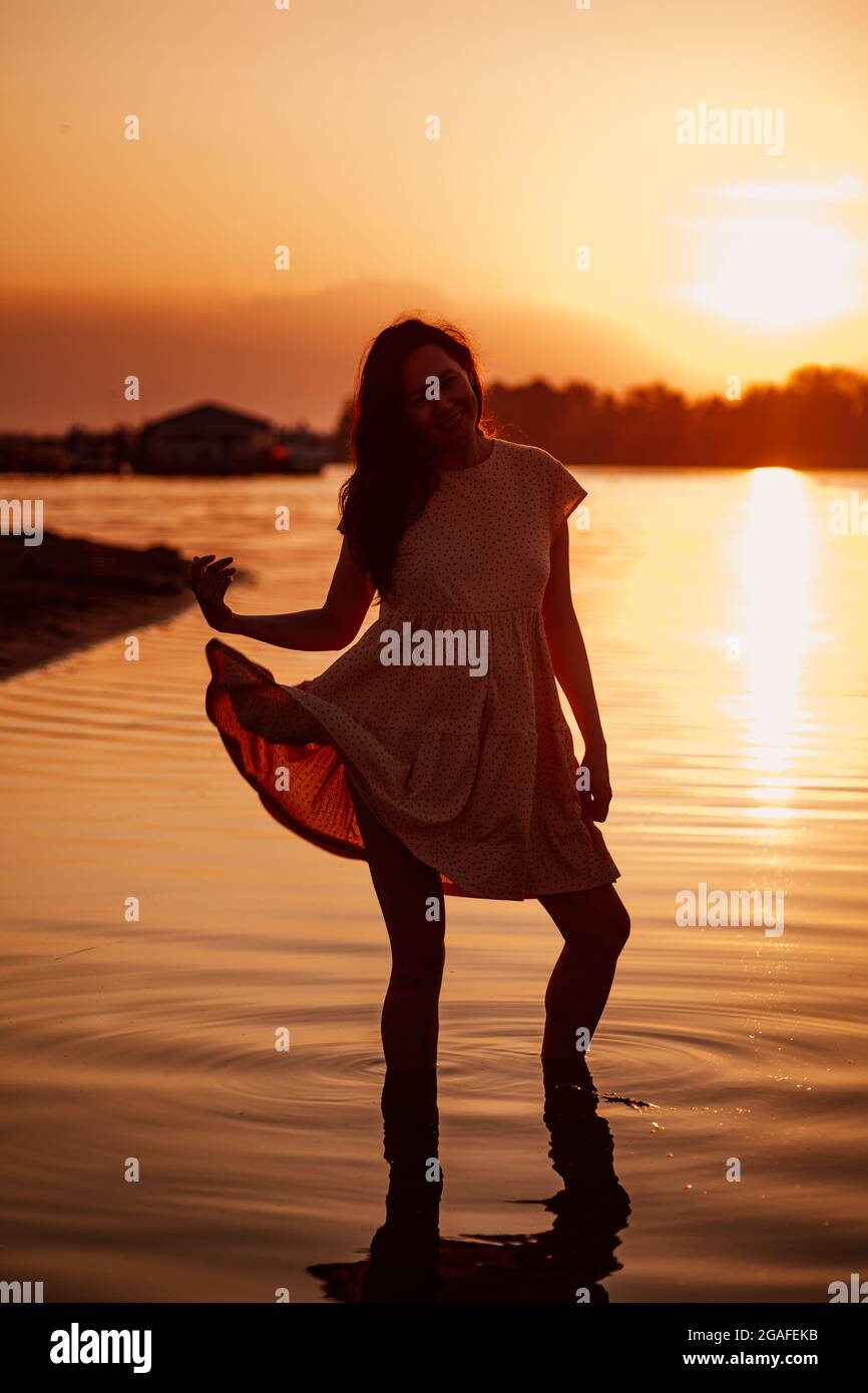 Jeune femme au coucher du soleil. Silhouette de bonne femme dans les rayons  du soleil couchant, debout sur la mer dans l'eau et jouant avec sa robe  Photo Stock - Alamy
