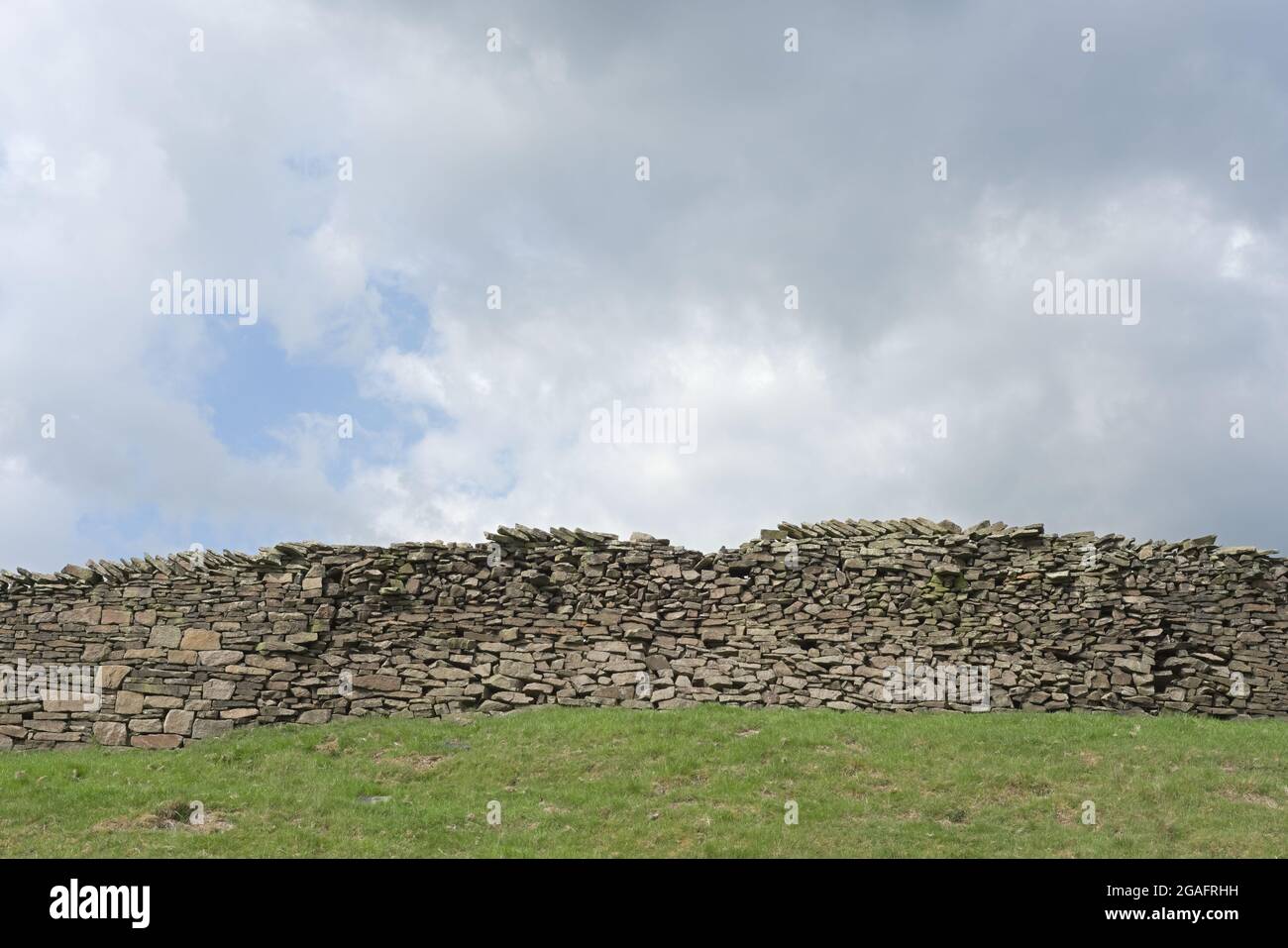 Grand mur en pierre sèche et fond bleu ciel fortement nuageux. Thème agricole et rural, champ vert herbacé en premier plan. Beaucoup d'espace de copie. Banque D'Images