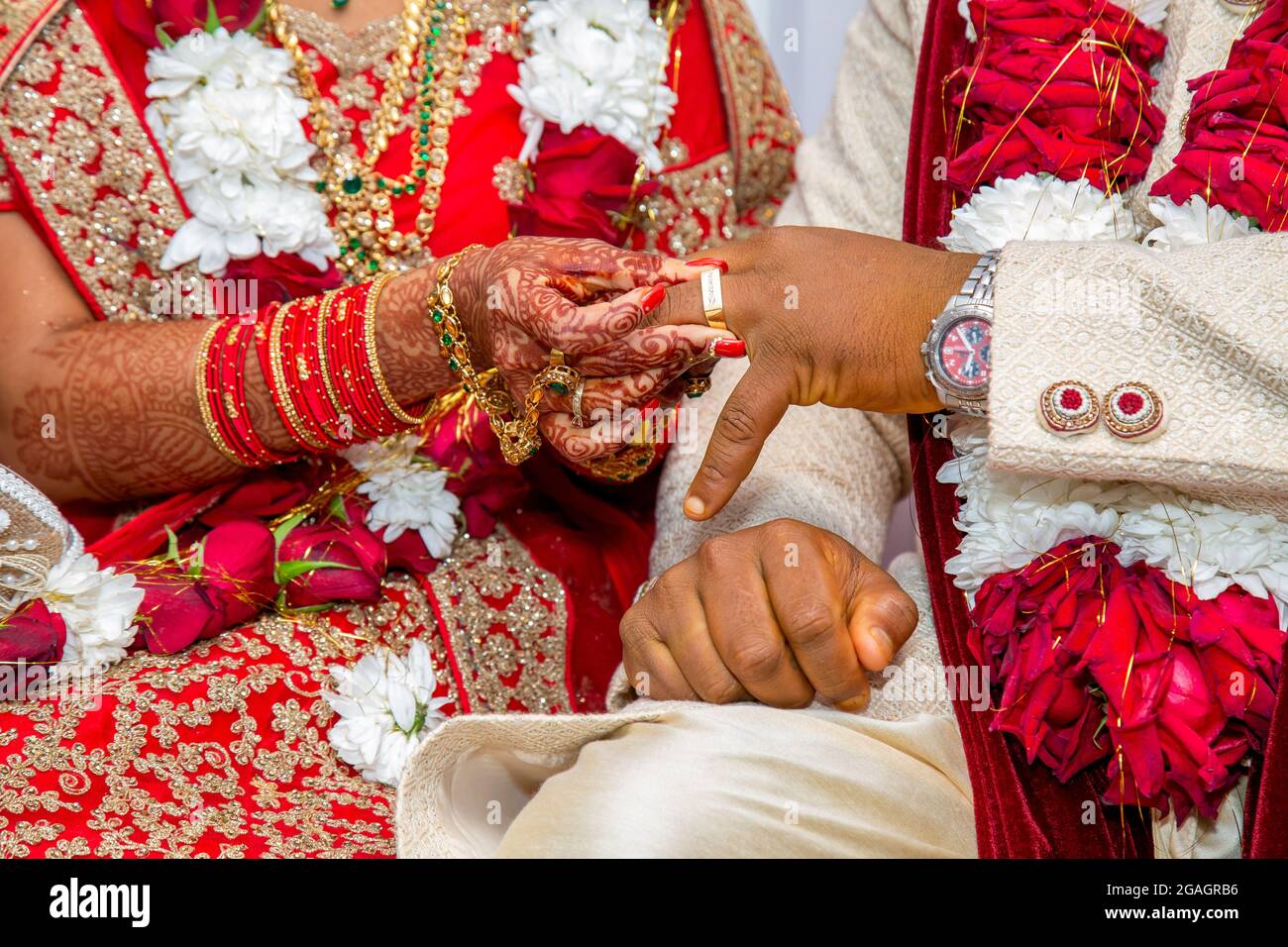 Mariée avec bijoux de mariée et décoration de henné sur sa main attache l'anneau au doigt du marié à la cérémonie religieuse traditionnelle lors d'un mariage hindou Banque D'Images