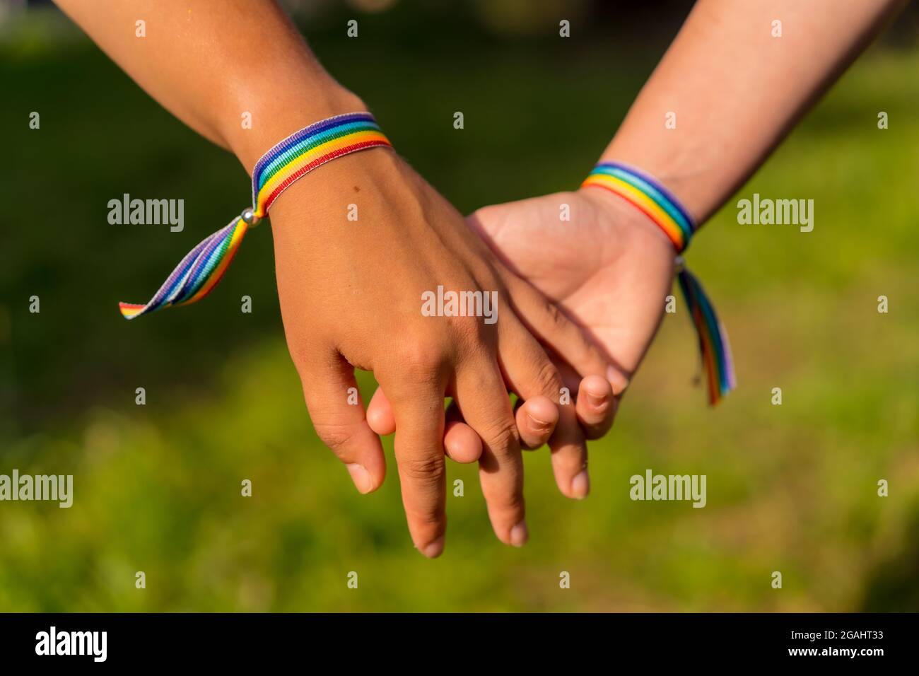 Gros plan de deux jeunes femmes caucasiennes tenant des mains avec des bracelets de fierté LGBT à l'extérieur Banque D'Images