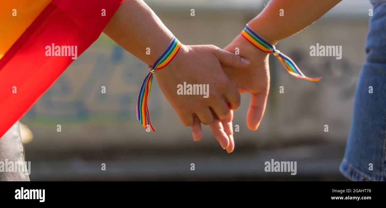 Photo panoramique de deux jeunes femmes caucasiennes tenant les mains avec des bracelets de fierté LGBT à l'extérieur Banque D'Images