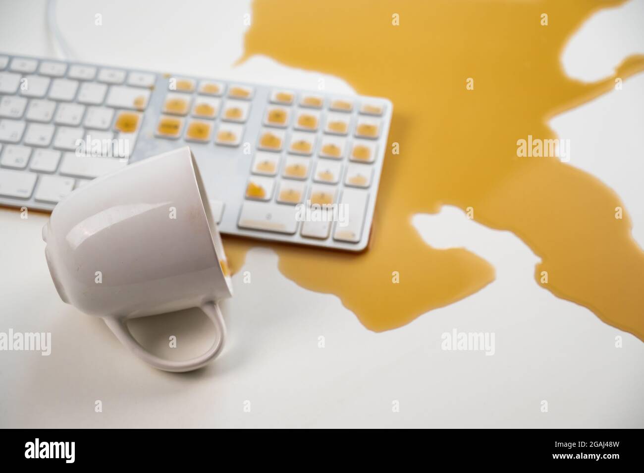 Tasse de café noir renversée sur le clavier de l'ordinateur sur la table blanche. Banque D'Images Tasse de café noir renversée sur le clavier de l'ordinateur sur la table blanche. Banque D'Images