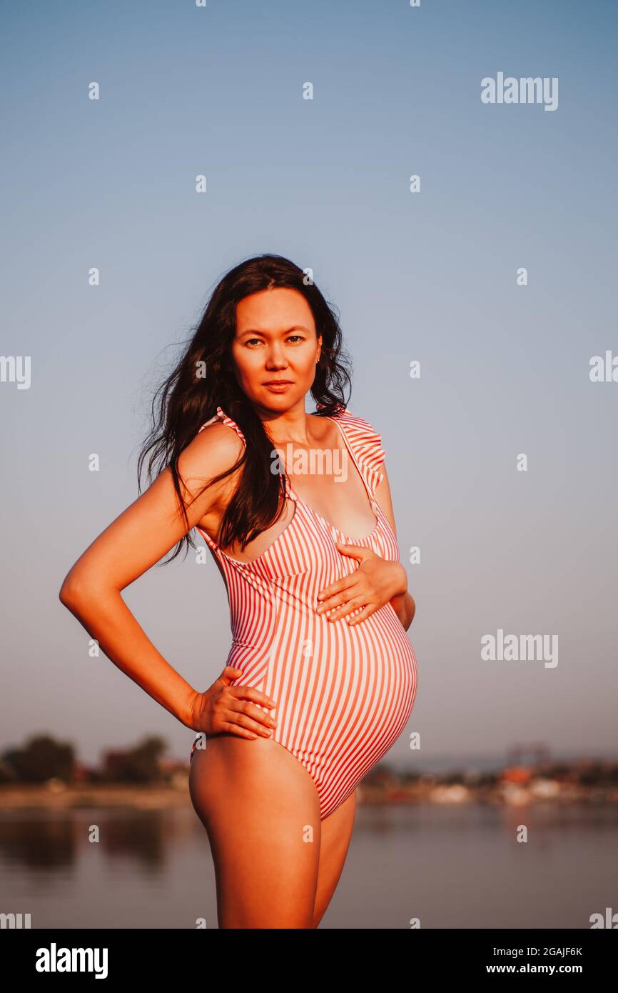 femme enceinte en maillot de bain, charmante, détendue femme enceinte en  maillot de bain rose avec une main à l'estomac sur la plage dans la lumière  orange du Photo Stock - Alamy