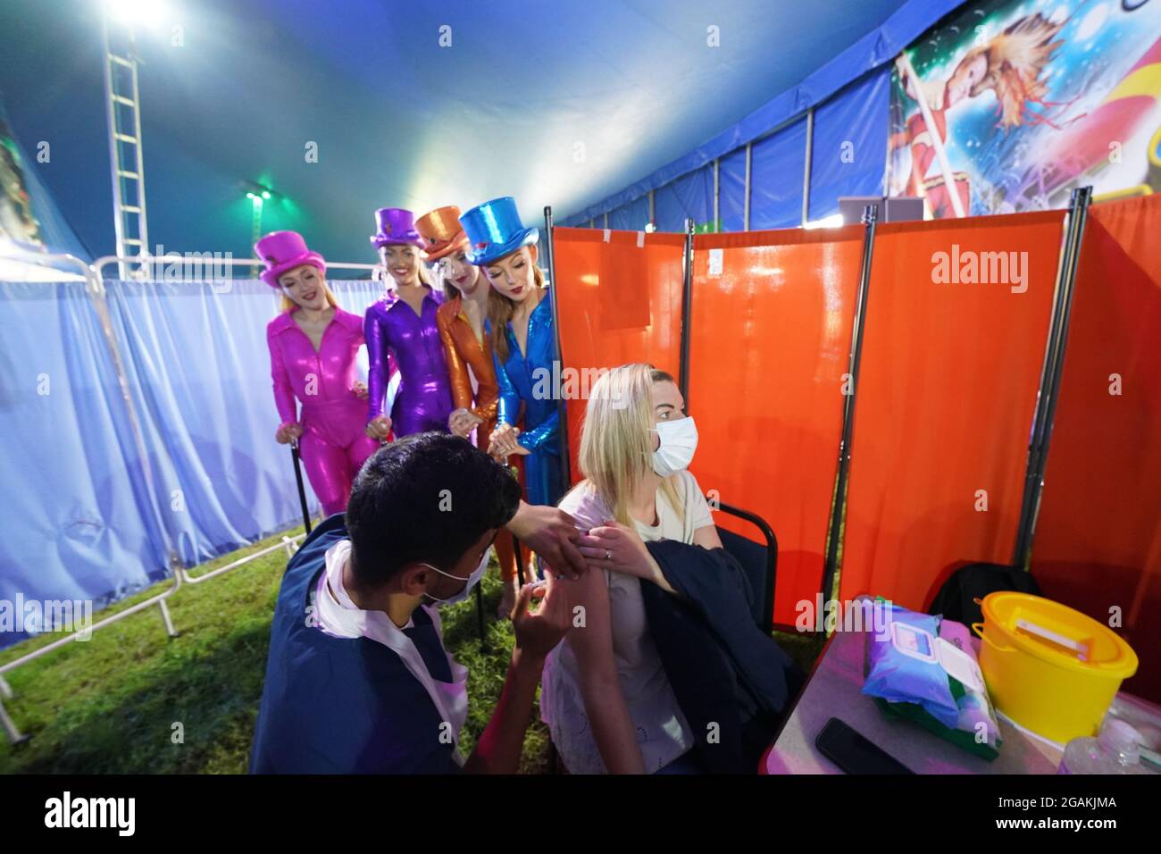 Des artistes de Circus Extreme regardent Rhiannon Alexander, 34 ans, de Bradford, recevoir une vaccination Covid-19 dans une clinique de vaccination pop-up dans le chapiteau du cirque de Halifax. Date de la photo: Samedi 31 juillet 2021. Banque D'Images