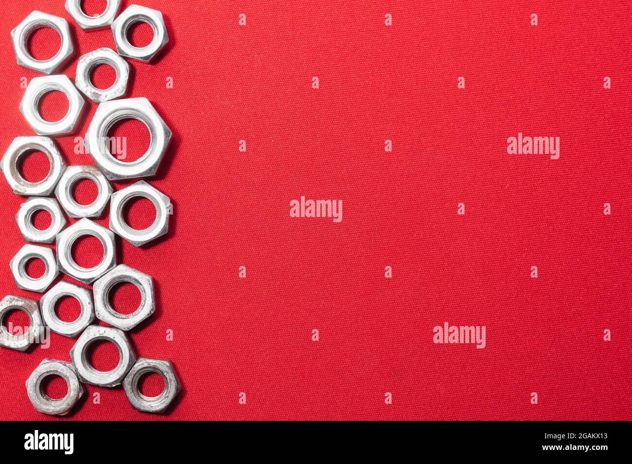 Écrous en acier sur fond rouge, côté gauche laissant de l'espace pour le texte publicitaire Banque D'Images