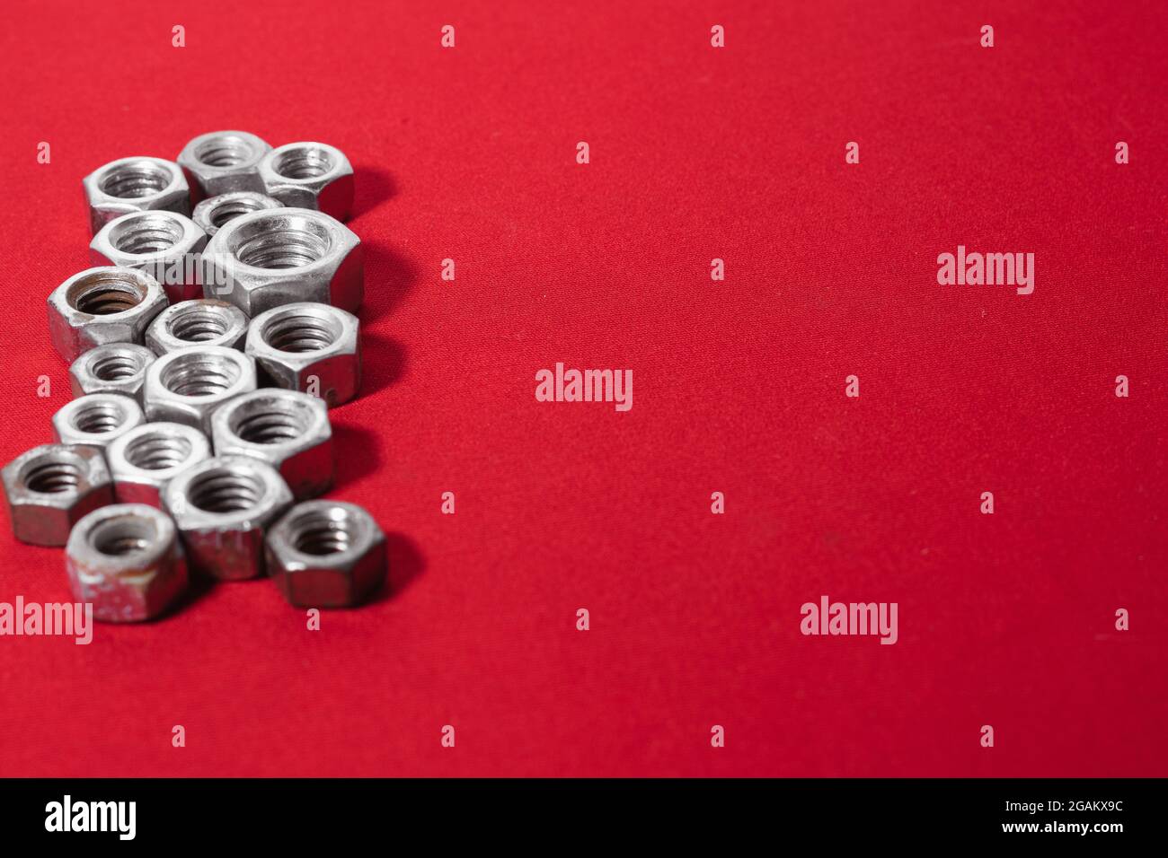 Écrous en acier sur fond rouge, côté gauche laissant de l'espace pour le texte publicitaire Banque D'Images