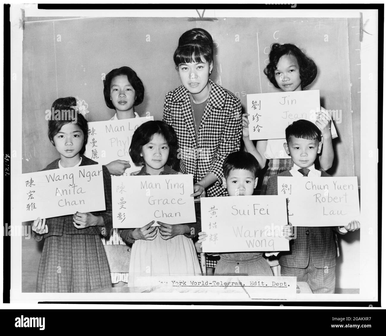 Mlle April Lou, enseignante au PS 1, Manhattan, avec six enfants chinois, arrivées récentes de Hong Kong et Formosa, qui tiennent des plaques indiquant son nom chinois (à la fois sous forme d'idéogrammes et de translittération) et le nom à inscrire dans les registres scolaires officiels, New York, NY, 1964. (Photo de Fred Palumbo/New York World-Telegram & Sun Collection/RBM Vintage Images) Banque D'Images