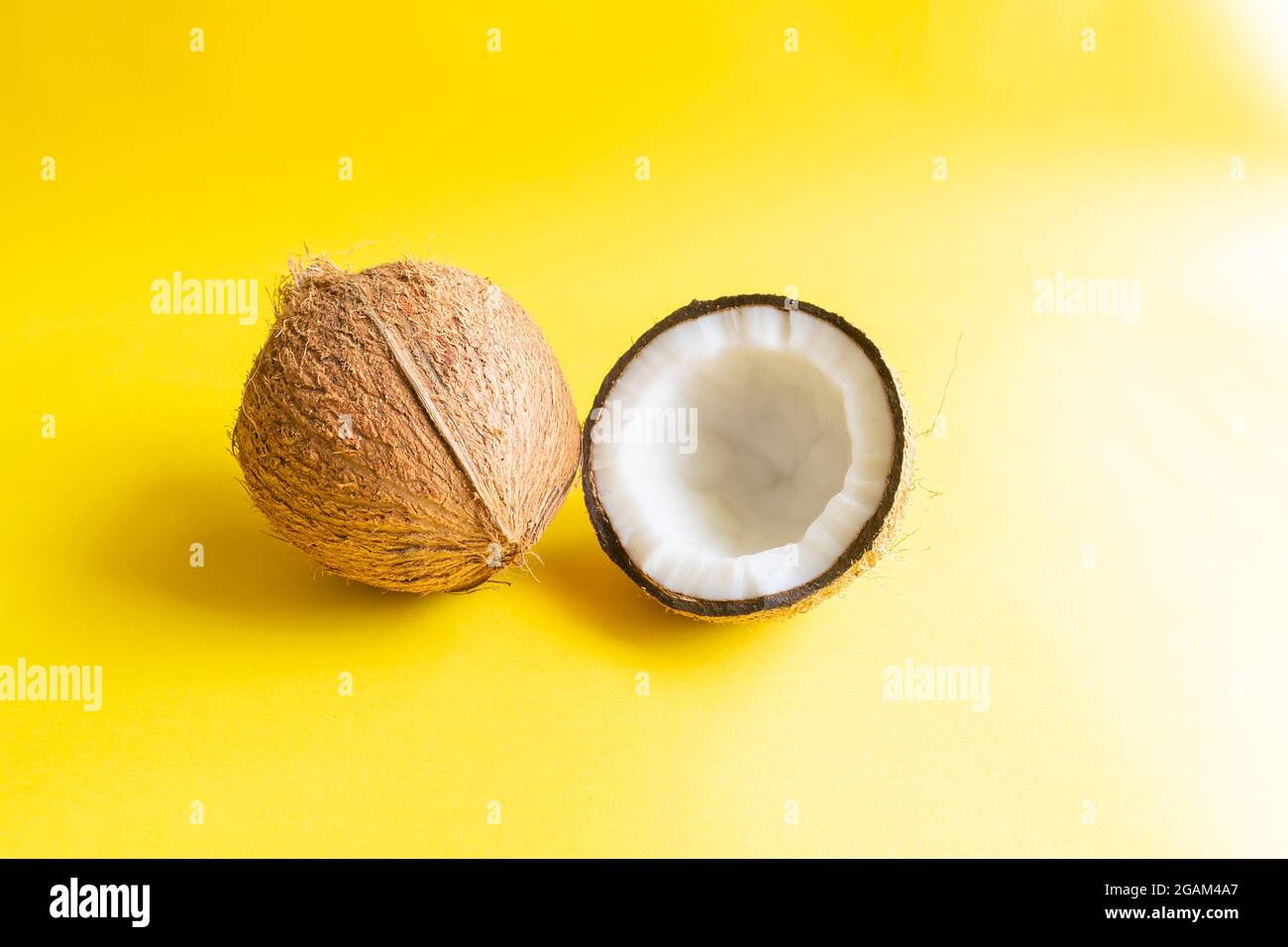 Noix de coco dont le husk enlevé et un demi-côté de la noix de coco avec la coquille sur le fond jaune et utilisé la focalisation sélective. Banque D'Images