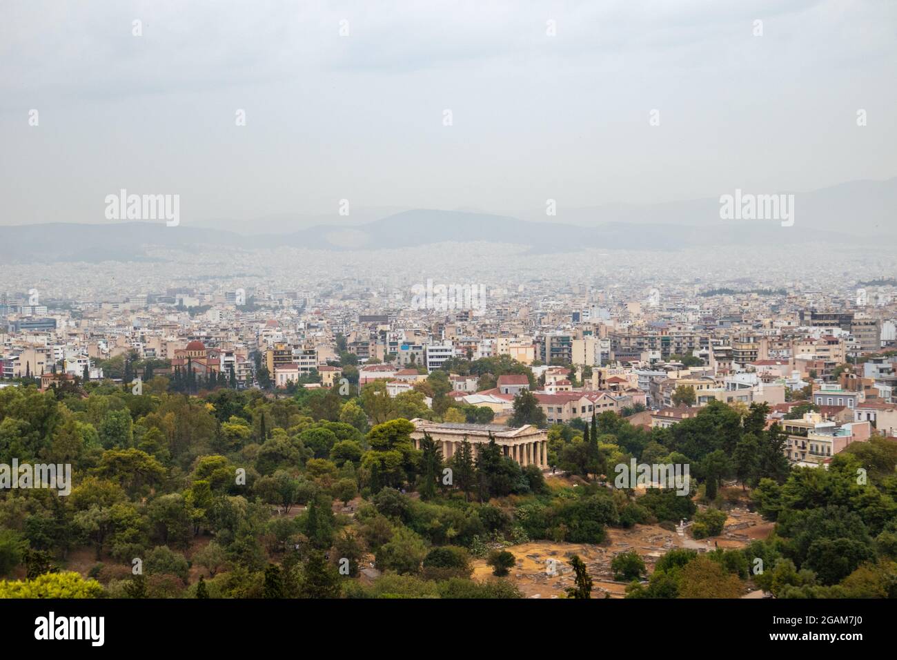 Vue sur le temple d'Hephaestus dans la verdure et l'ancien centre-ville d'Athènes avec des bâtiments blancs sur les jours de brouillard gris depuis la colline d'Areopagus près de l'Acropole Banque D'Images