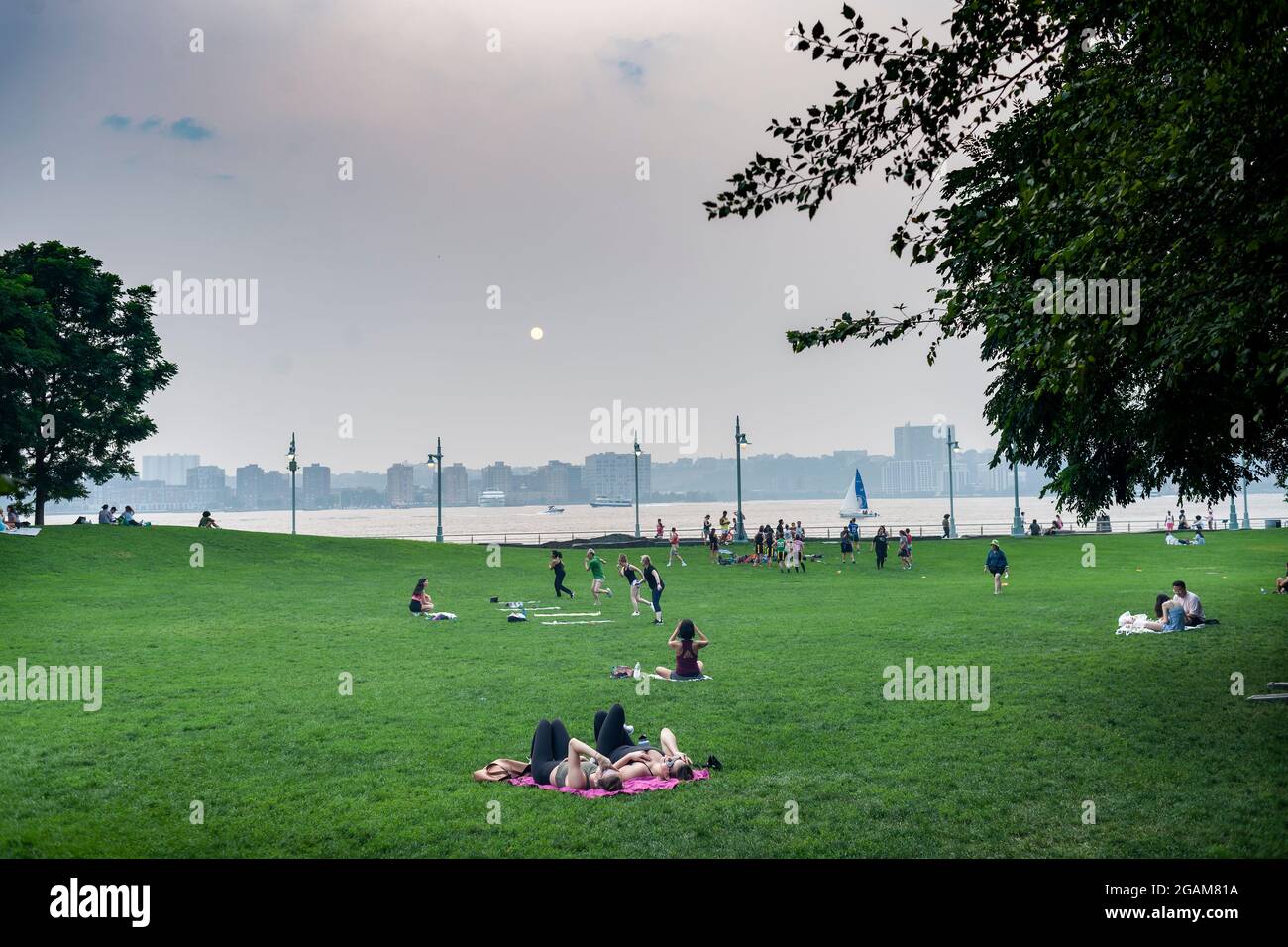 Les gens s'exercent et se détendent dans le parc de la rivière Hudson sous un soleil rouge au coucher du soleil à New York le mardi 20 juillet 2021. La fumée des feux de forêt au Canada et dans l'ouest des États-Unis se déforme et cause la brume et une qualité de l'air plus faible (© Richard B. Levine) Banque D'Images