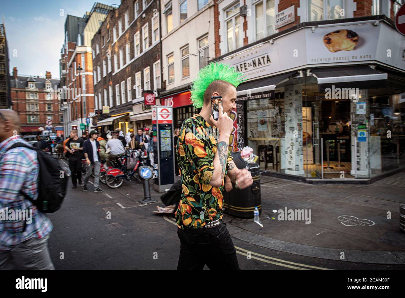 Punk avec mohawk vert marchant avec le téléphone mobil sur Old Compton Street dans Soho de Londres après avoir mis fin à toutes les restrictions liées au coronavirus Banque D'Images