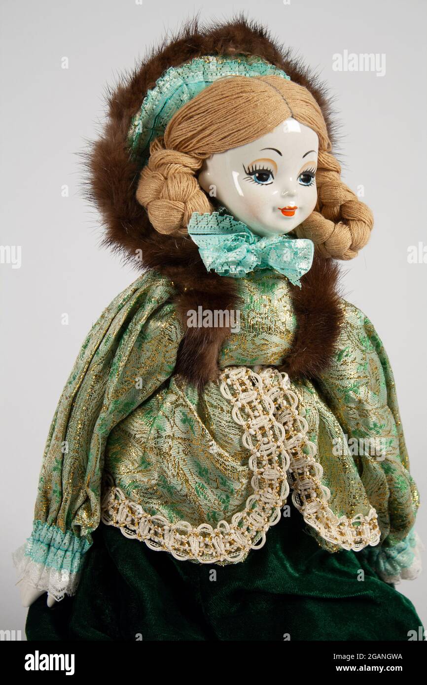 une poupée en porcelaine décorative avec un visage peint, une bordure en fourrure et une casquette en dentelle dans une robe en brocart vert et en velours sur un fond gris doux avec une touche de copie Banque D'Images
