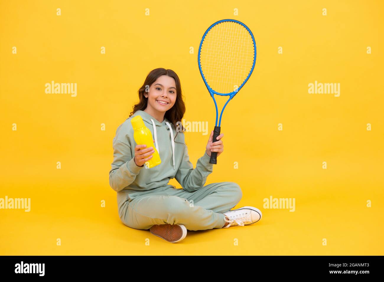 un enfant heureux tient une raquette de badminton et boit l'eau de la bouteille sur fond jaune, santé. Banque D'Images