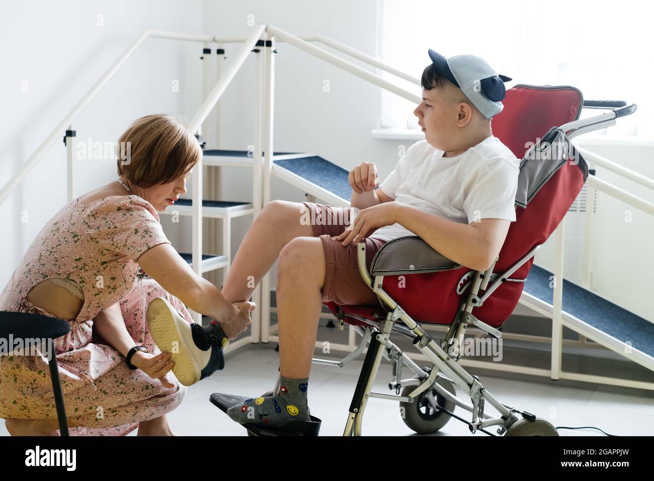 Mère aidant un garçon handicapé de 17 ans en fauteuil roulant avec paralysie cérébrale à mettre des chaussures, avant d'aller pour une promenade. Femme aide la personne avec spécial Banque D'Images