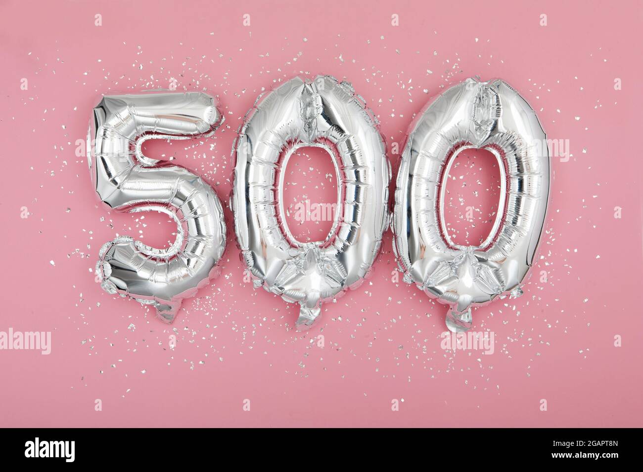 De dessus de ballons brillants argentés démontrant le numéro 500 sur fond rose avec paillettes éparpillées Banque D'Images