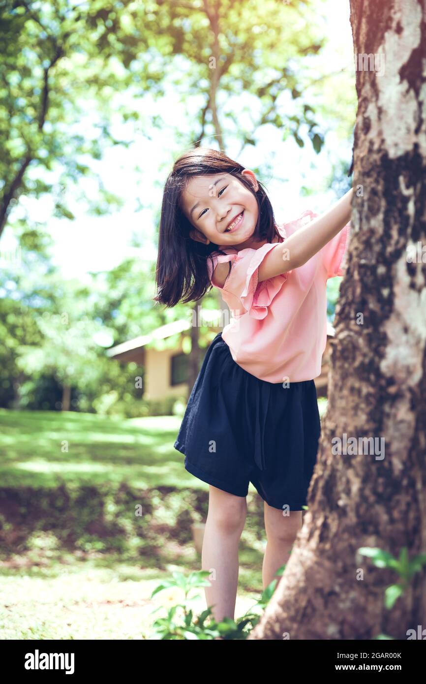 Jolie petite fille asiatique sous un gros arbre à l'extérieur dans le parc. Banque D'Images