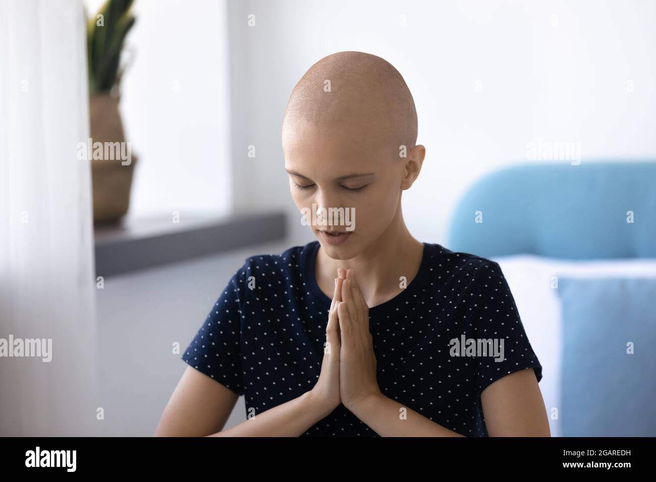 Bonne jeune femme sans cheveux priant avec les mains pliées. Banque D'Images