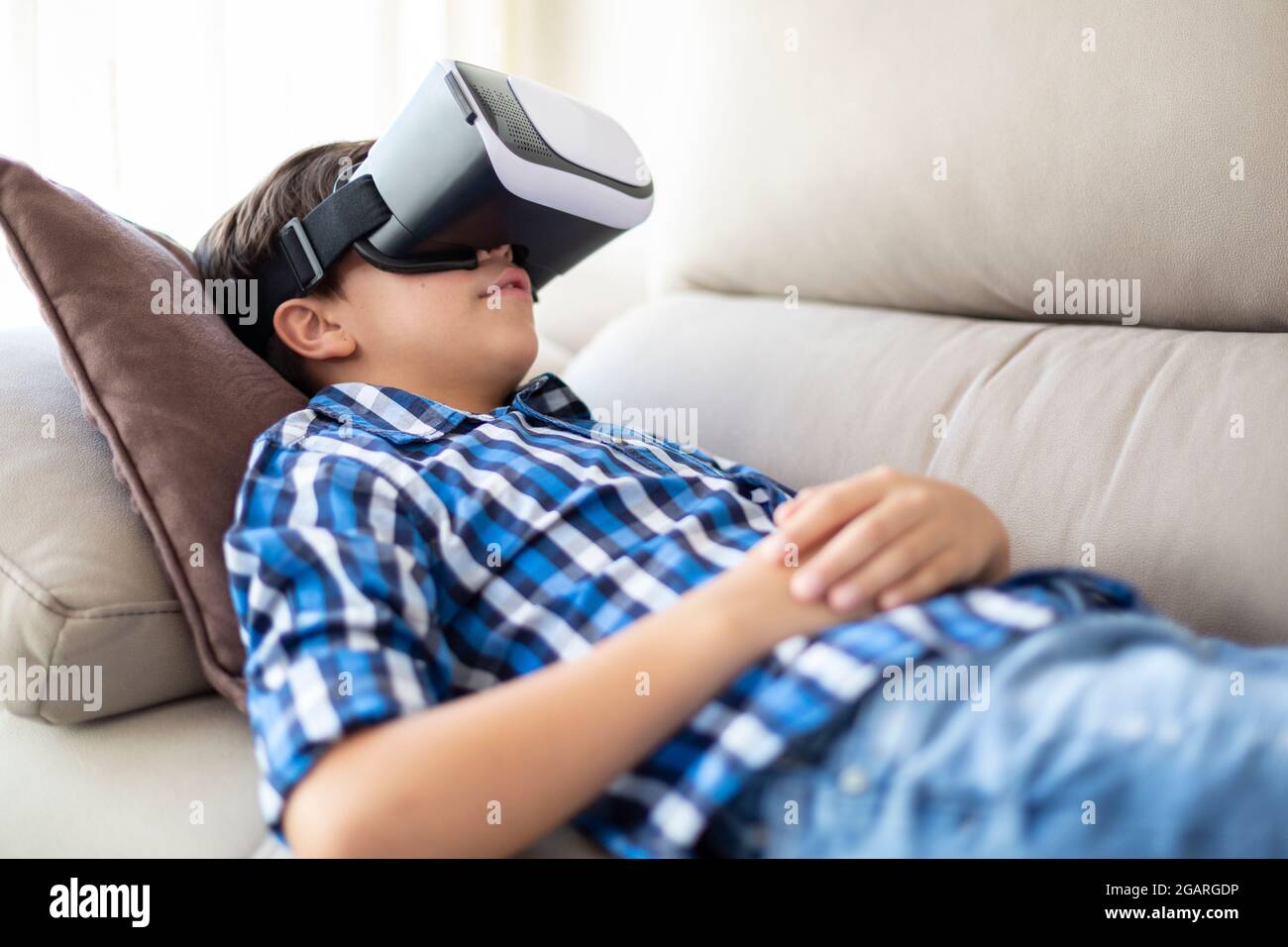 Adolescent appréciant l'expérience de réalité virtuelle couché sur le canapé à la maison. Banque D'Images
