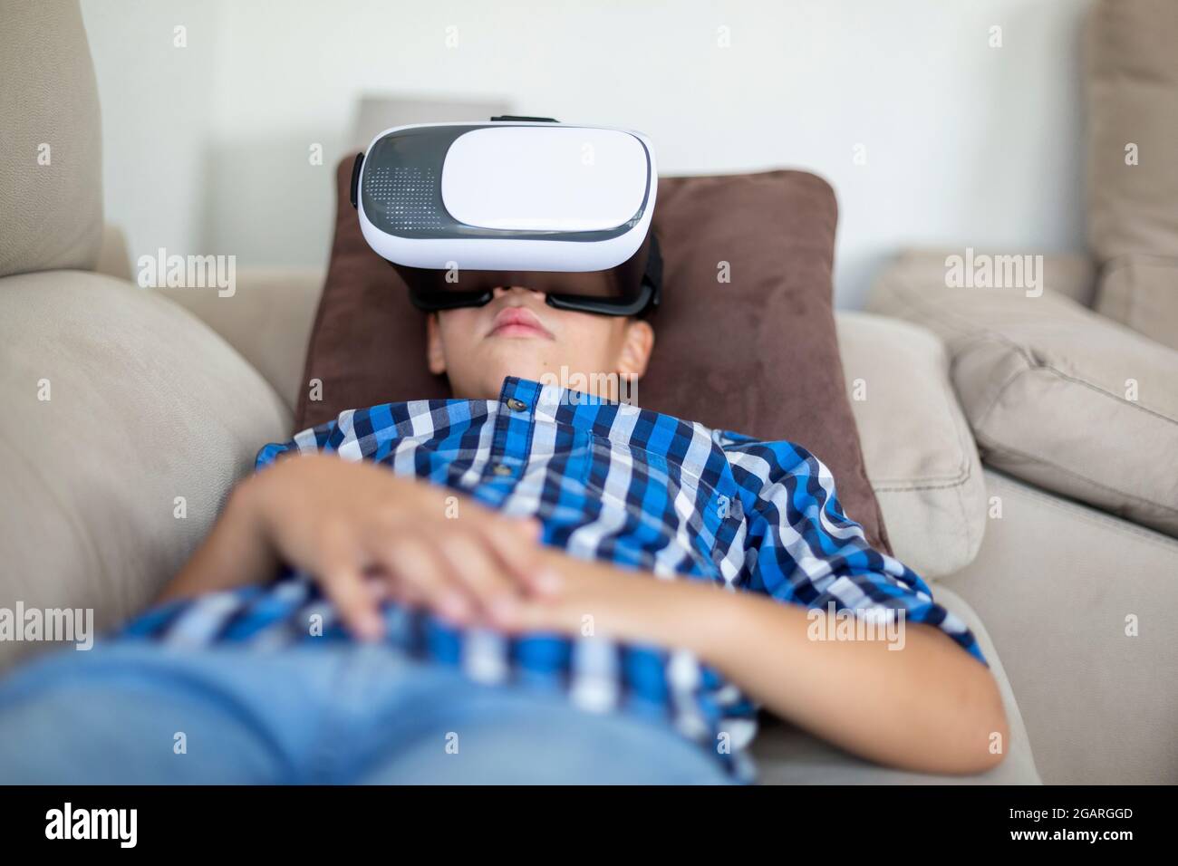 Garçon caucasien couché confortablement sur le canapé à la maison. Il utilise des lunettes de réalité virtuelle. Banque D'Images