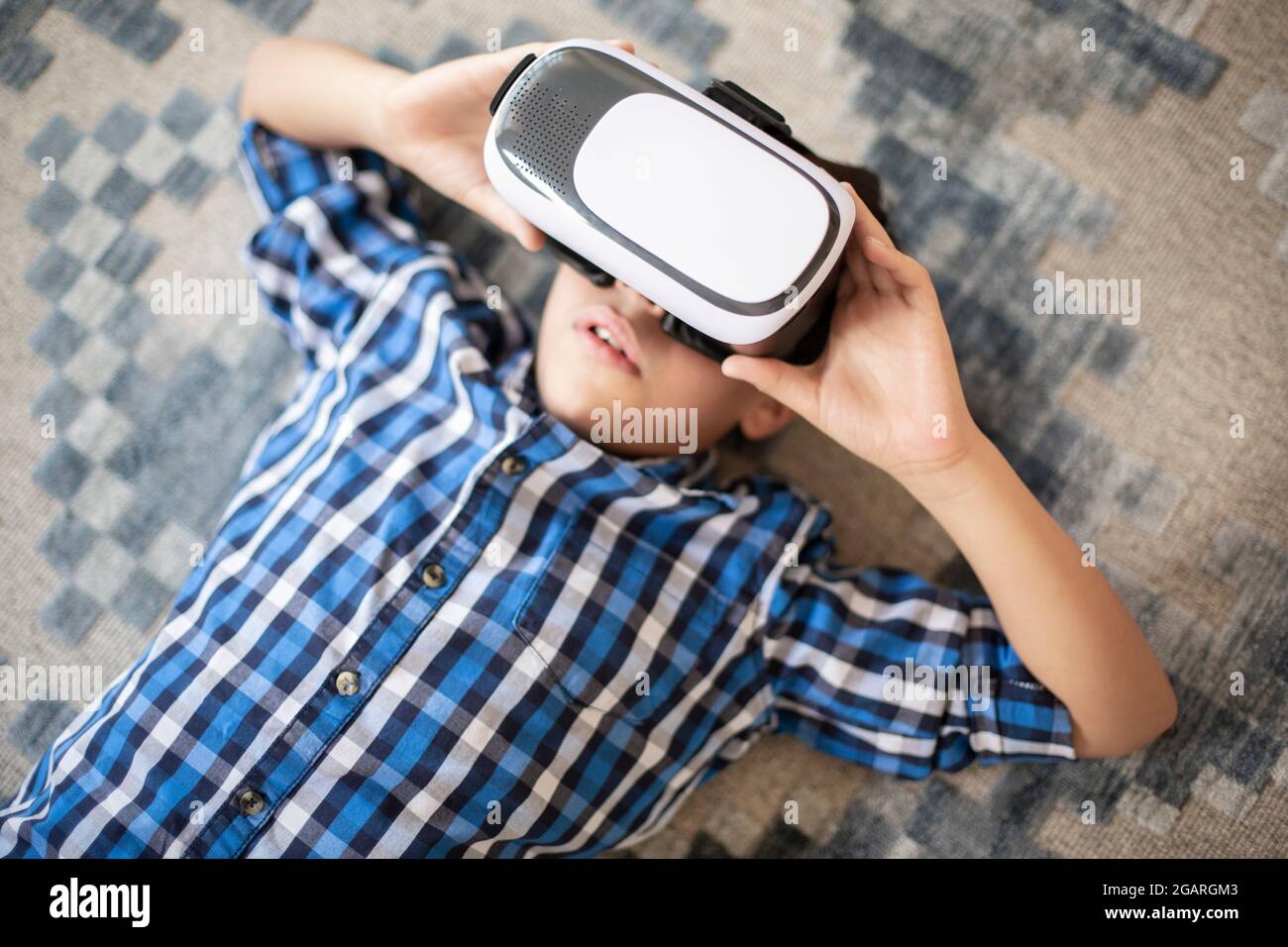 Gros plan d'un adolescent caucasien excité appréciant la réalité virtuelle. Il est allongé sur le tapis. Banque D'Images